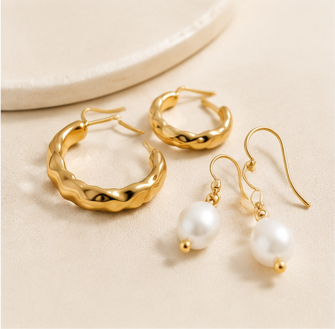 Gold-tone hoop and pearl earrings on a warm beige background