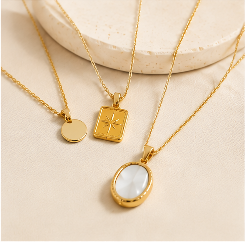 Gold-tone pendant necklaces displayed on a warm neutral background
